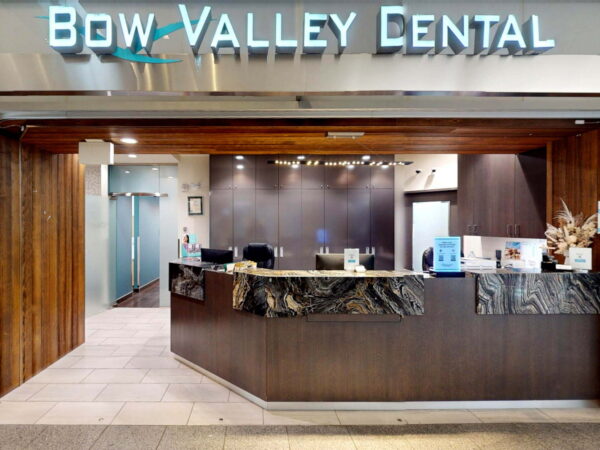 Reception area of Bow Valley Dental featuring a modern counter, wooden accents, and a welcoming atmosphere. The sign prominently displays the practice name, and the space is well-lit and organized.