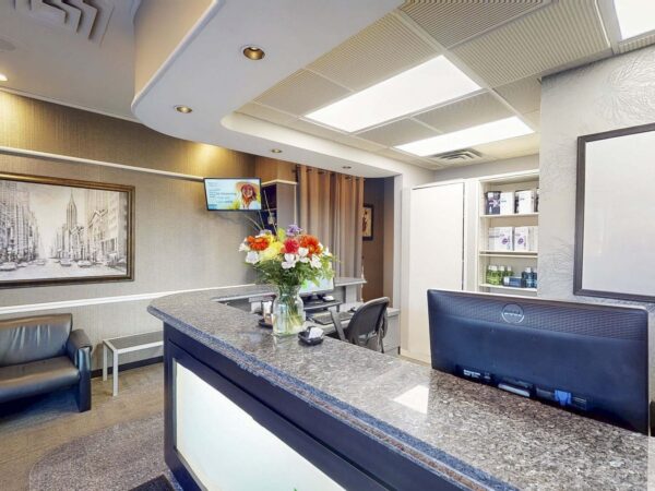 A modern reception area featuring a polished granite counter, a flower arrangement, seating for visitors, and decorative wall art. A screen displays information, contributing to a welcoming atmosphere.