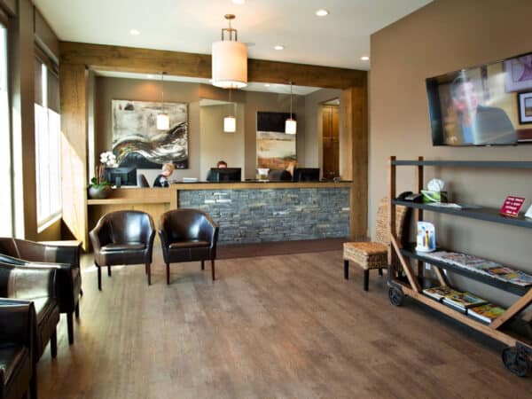 A modern dental office reception area featuring a welcoming front desk, comfortable chairs, and a display shelf with magazines. Natural light fills the space, creating a warm atmosphere, perfect for patients waiting for their appointments.