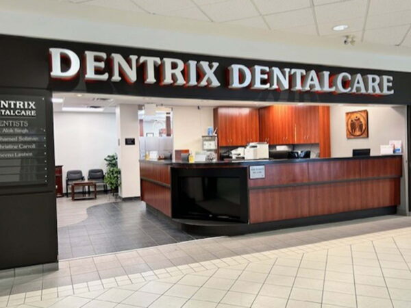 Reception area of Dentrix Dentalcare, featuring a wooden front desk, a sign above, and a welcoming atmosphere. The space includes a lobby with seating and informational displays.