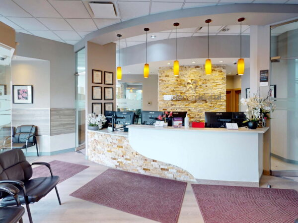 A modern reception area featuring a stylish front desk with decorative lighting, surrounded by comfortable seating and elegant decor. The space is well-lit and inviting, with warm colors and contemporary design elements.