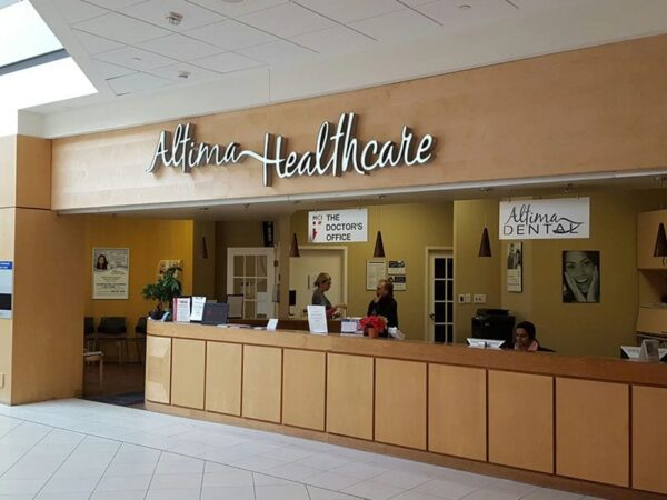 A reception area of a healthcare facility, featuring a wooden counter with staff members, a welcoming sign that reads "Atrium Healthcare," and various informational posters on the walls.