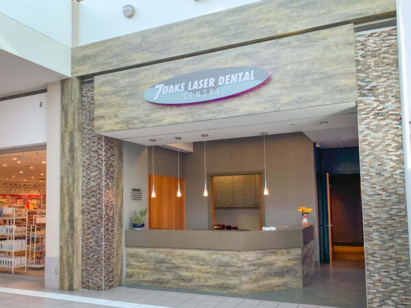 A modern dental office reception area is displayed, featuring a clean, stylish design with a stone facade and a sleek counter. The sign reads "Trent's Laser Dental," indicating a focus on advanced dental services. The space is well-lit and welcoming.