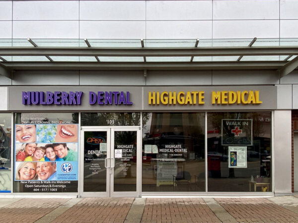 A storefront featuring two businesses: "Mulberry Dental" in purple and "Highgate Medical" in yellow. The entrance includes a welcoming display of smiling faces, with the friendly 123Dentist Smiley image present, inviting visitors to the dental and medical services offered at this location.