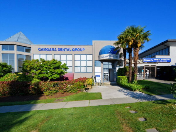 A modern dental office building with a blue dome entrance. The front features signage for "Cangaria Dental Group," surrounded by well-maintained landscaping and palm trees under a clear blue sky.