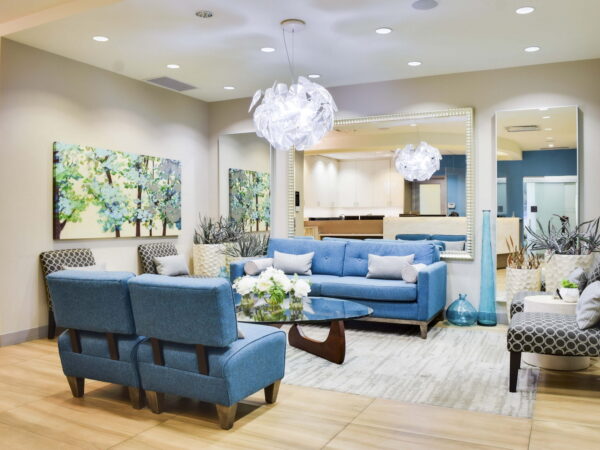 A modern, inviting lounge area featuring a blue sofa set, cozy armchairs, and artistic wall decor. Bright, natural lighting enhances the space, complemented by decorative plants and stylish light fixtures, creating a welcoming atmosphere.