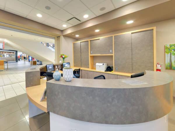 A modern dental reception area featuring a curved front desk, equipped with computers and decorative elements like a vase of flowers. The space is well-lit and inviting, designed for a comfortable patient experience.