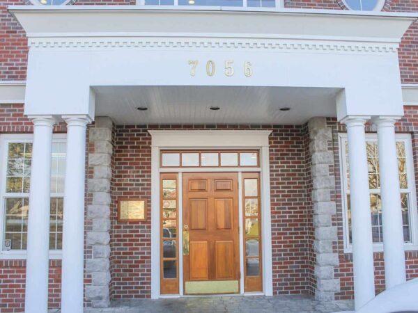 A close-up view of a brick building entrance featuring a wooden double door flanked by decorative columns. The structure is adorned with a sign above the door displaying the numbers "2030." Natural light illuminates the scene.