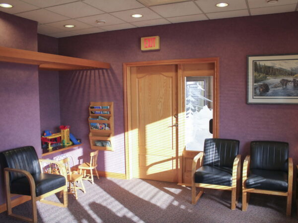 A waiting area features purple walls, wooden furniture, and three black chairs. A small children's play area includes toys and a bright window. A painting of a landscape is hung on the wall.