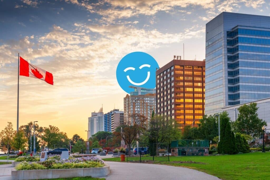 A vibrant sunset view of a city skyline featuring modern buildings, a Canadian flag, and a smiling blue icon overlay, highlighting a sense of positivity in a public park setting.