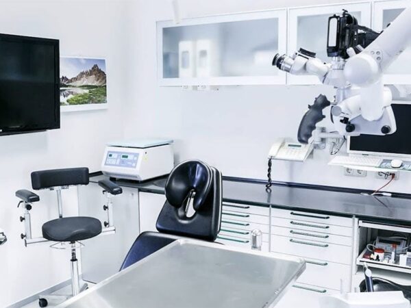 A modern dental clinic featuring a patient chair, dental instruments on a counter, and a monitor on the wall. The setting is clean and well-lit, suggesting a professional environment for dental procedures.