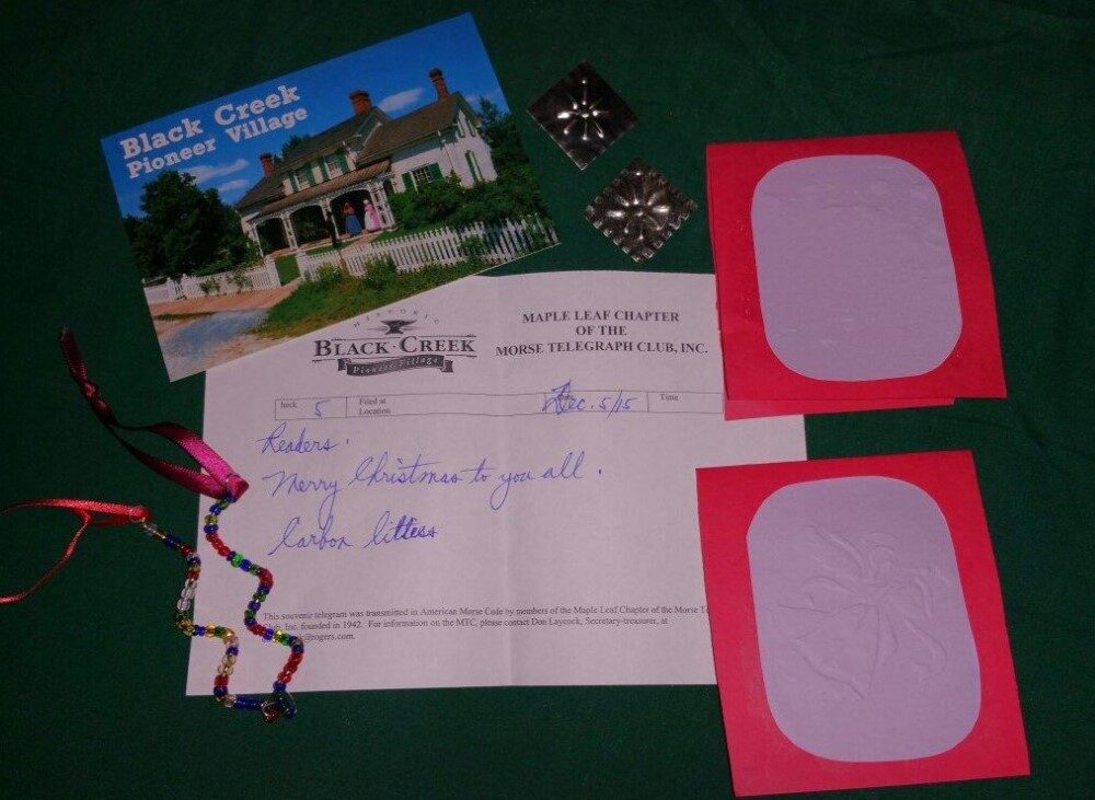 A collection of items arranged on a green surface, including a postcard from Black Creek Pioneer Village, a letter, two colorful blank cards, and decorative ribbon. The postcard features a historic building, while the letter expresses greetings.