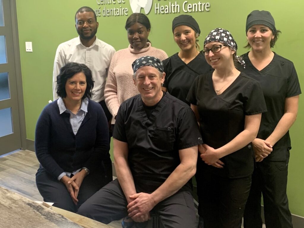 A group of healthcare professionals, including a dentist and support staff, pose together in a clinic. They wear black scrubs and matching head coverings. The environment appears friendly and welcoming, promoting a sense of teamwork and care in a pediatric health center.