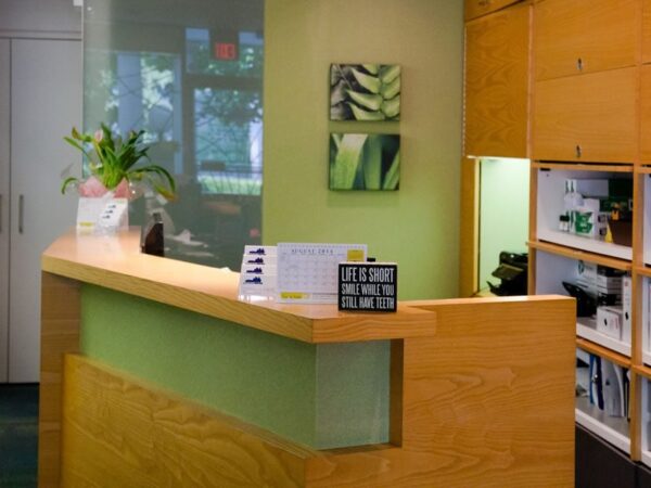 A modern reception area with a wooden desk, green walls, decorative plants, and organized shelves filled with binders.