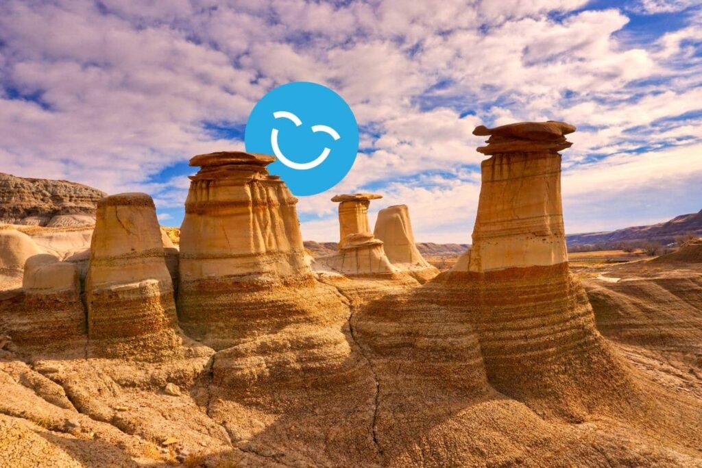 Rock formations, known as hoodoos, in a desert landscape under a partly cloudy sky with a smiling emoji in the foreground.