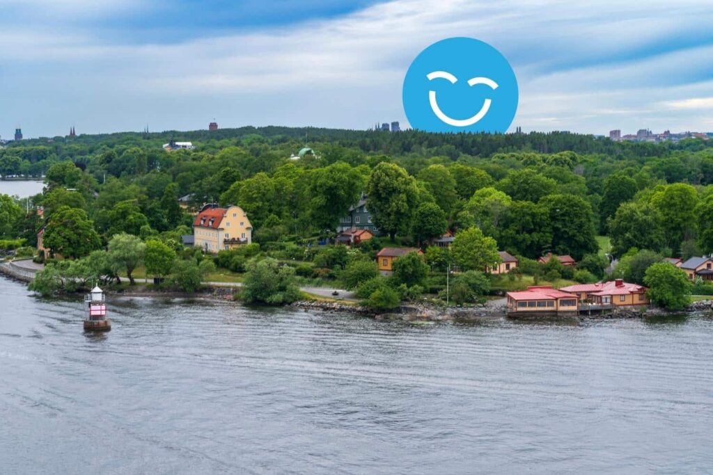 A serene waterscape features a lush green shoreline dotted with colorful homes. A small boat glides along the calm water under a cloudy sky, while a blue smiley face icon adds a cheerful element to the scene.