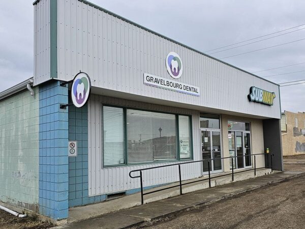 A gray building with a corrugated metal facade, featuring a sign for "Gravel Mortgage Centre" and another for "Kids Drop." The entrance has a ramp and large windows. The surrounding area appears empty and industrial.