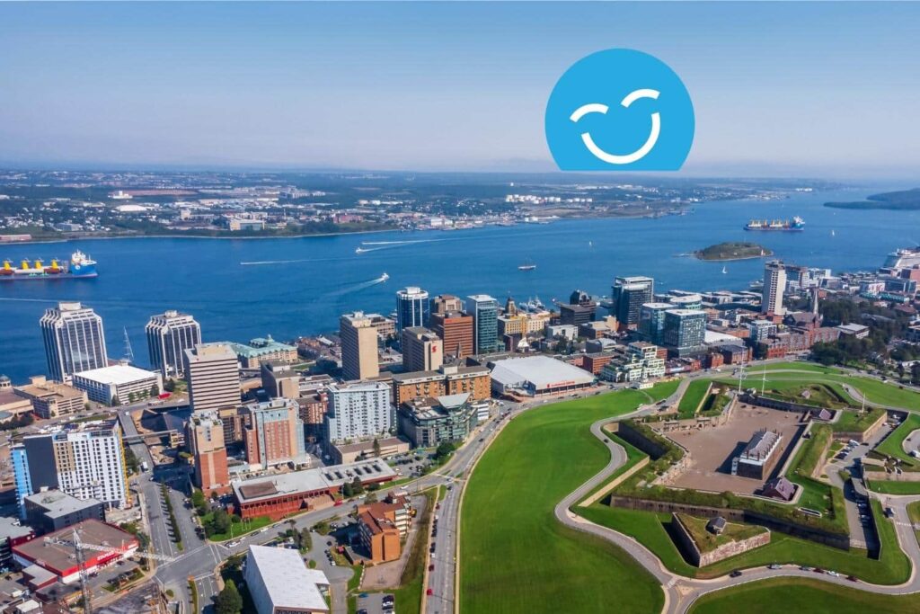 Aerial view of a vibrant cityscape by the waterfront, featuring tall buildings and green spaces. In the sky, a blue smiley face icon adds a cheerful touch to the scene, capturing a lively urban atmosphere.
