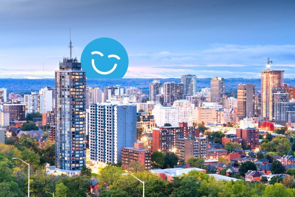 A city skyline at dusk featuring modern buildings, with a blue smiley face graphic overlay. The scene reflects a blend of urban architecture and natural greenery, conveying a vibrant and lively atmosphere.