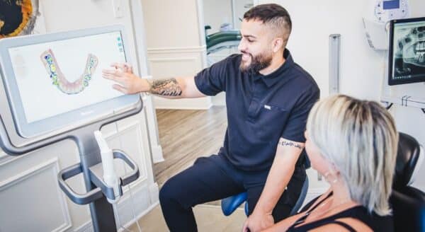 A dental professional discusses treatment options with a patient while pointing at a digital display. The bright and welcoming office environment suggests a friendly atmosphere, making it a comfortable space for dental consultations.