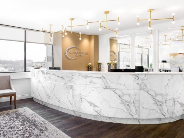 A modern reception area featuring a curved marble counter, stylish lighting fixtures, and large windows. Two chairs and a decorative rug are visible, creating an inviting atmosphere in a bright and contemporary space.