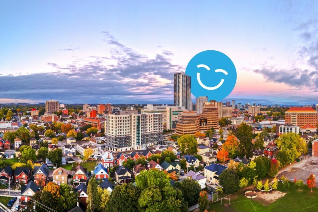 A picturesque urban skyline at sunset, showcasing a mix of modern buildings and residential areas. Vibrant fall foliage and a blue smiley face graphic superimposed enhance the scene, indicating a cheerful atmosphere.