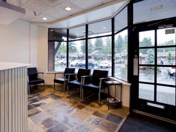 A modern waiting area featuring several black chairs, a large front window, and a tiled floor. Natural light streams in, illuminating the space, while a view of an overcast landscape is visible outside.