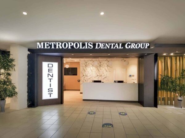 Reception area of Metropolis Dental Group, featuring a modern design with a white service counter, signage indicating "DENTIST," and indoor plants for a welcoming atmosphere.
