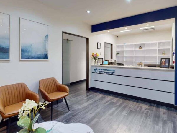 A modern reception area featuring two stylish brown chairs, a white counter with shelves, and abstract wall art. The space is well-lit with a blue accent wall, creating a welcoming atmosphere.
