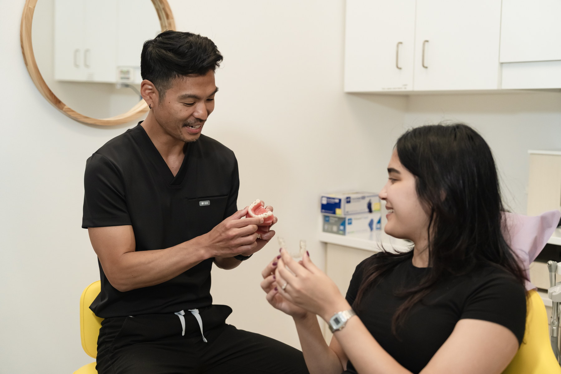 A dental professional and a patient sit together in a bright clinic, discussing dental care. The practitioner holds a model while the patient attentively engages, showcasing a friendly and informative atmosphere.