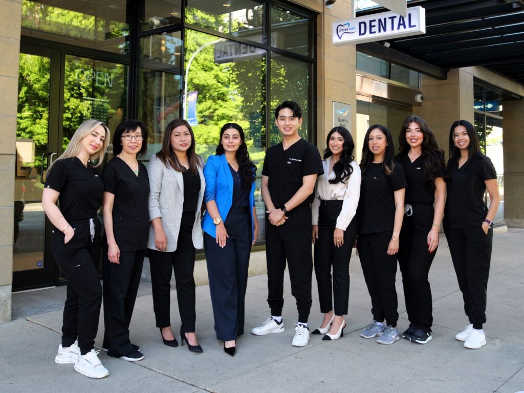 A diverse group of dental professionals stands outside a dental clinic, dressed in black scrubs. They smile and pose together, showcasing team spirit and approachability. In the background, the clinic's sign is visible.