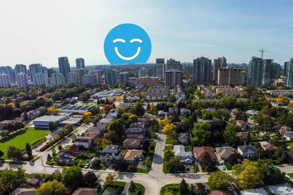 Aerial view of a suburban neighborhood with various houses, trees, and green spaces, contrasted by a skyline of urban buildings in the background. A large blue smiley face graphic is prominently displayed above the scene.