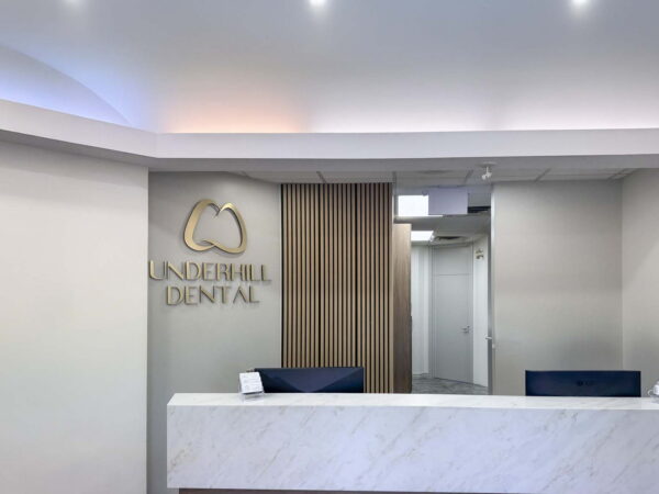 A modern dental reception area featuring a marble-front desk, blue chairs, and a stylish wall with the "Underhill Dental" logo. Soft lighting enhances the contemporary ambiance, creating a welcoming atmosphere for patients.