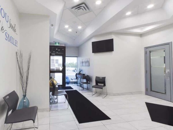 A modern, well-lit reception area featuring white walls, a sleek floor, and minimalistic decor. Seating is arranged along the walls, and a large window provides natural light. A welcome message is displayed on the wall, complementing the professional atmosphere.