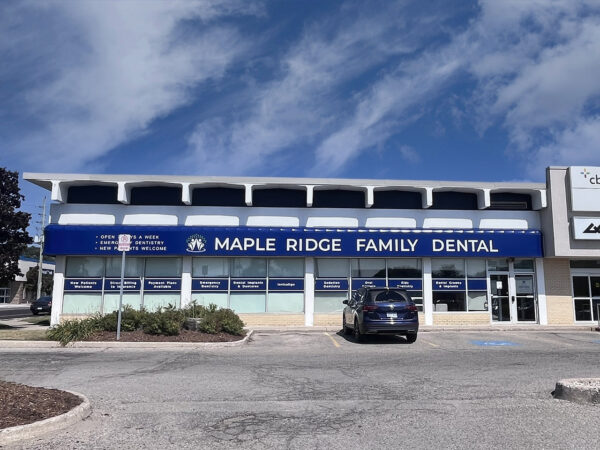 A dental clinic called Maple Ridge Family Dental is displayed in a modern building, featuring a blue and white exterior with large windows. The area is clear, showcasing a parked car and a bright sky above.