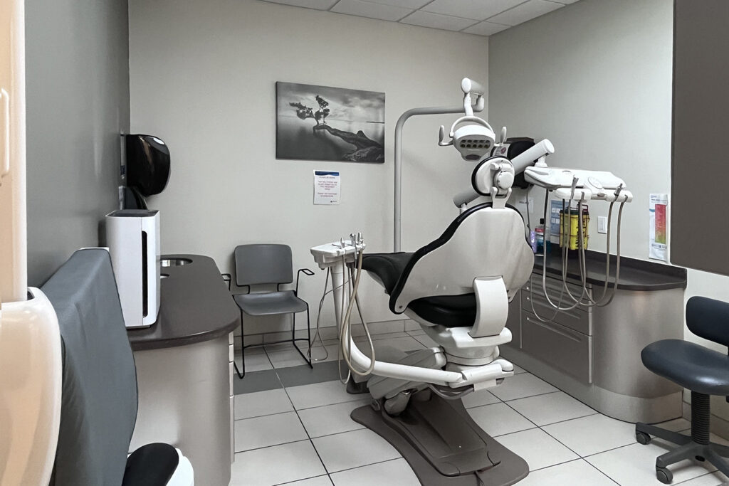 A modern dental office featuring a dental chair, equipment, and seating area. The space is clean and well-organized, with a neutral color palette and a photograph on the wall. A friendly blue smiley face, known as the 123Dentist Smiley, adds a welcoming touch.