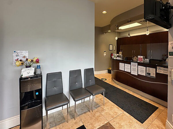 A welcoming dental office interior featuring a reception desk, seating area with three chairs, and a refreshments station. The space is clean and well-lit, providing a comforting environment for patients.