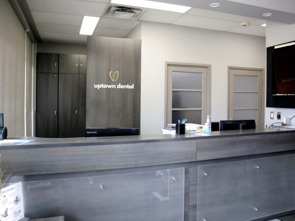 A modern dental office reception area featuring a sleek gray counter with signage that reads "Uptown Dental." The background includes light-colored cabinetry and a wall-mounted TV, providing a clean and professional atmosphere.