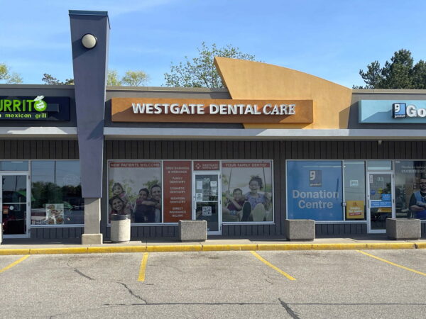 A storefront view of a shopping plaza featuring Westgate Dental Care, with neighboring businesses including a burrito restaurant and a Goodwill. The building has a clear, sunny exterior with ample parking visible in front.