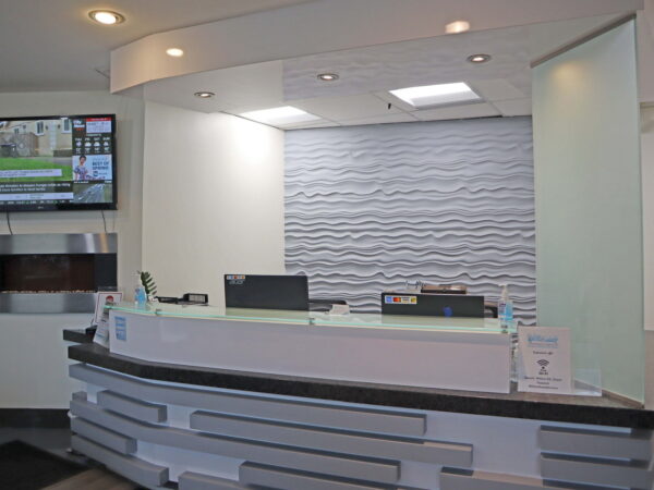 A modern reception area featuring a sleek, curved front desk, a textured wall behind, and a television displaying information. The space is well-lit and inviting, designed for welcoming visitors.