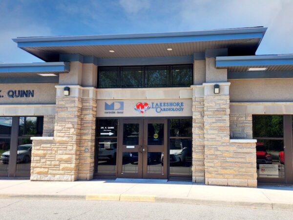 A modern building entrance featuring large glass doors and a stone façade, with signage for "Lakehouse Centre" and "Dr. K. Quinn" prominently displayed. The setting is bright, and trees are visible in the background.