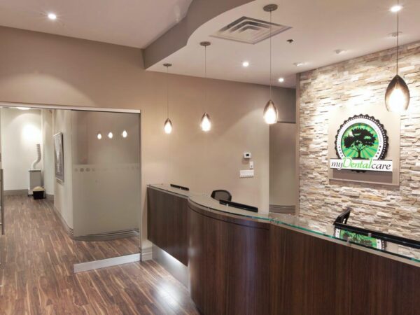 A modern dental office interior featuring a welcoming reception area with wood accents, stone walls, and soft lighting. The space is designed for comfort and includes the friendly 123Dentist Smiley logo on the wall, creating a friendly atmosphere for patients.