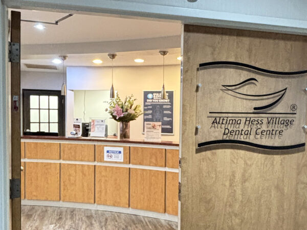 A welcoming entrance to the Allina Health Village Dental Centre featuring a wooden reception desk and floral arrangements. The interior is brightly lit, creating an inviting atmosphere for patients.
