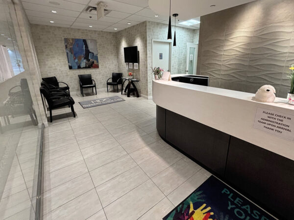 A modern dental office reception area featuring a sleek front desk, contemporary chairs, and vibrant decor, including flowers. The space is well-lit and welcoming, designed for patient comfort. A friendly 123Dentist Smiley adds a cheerful touch to the environment.