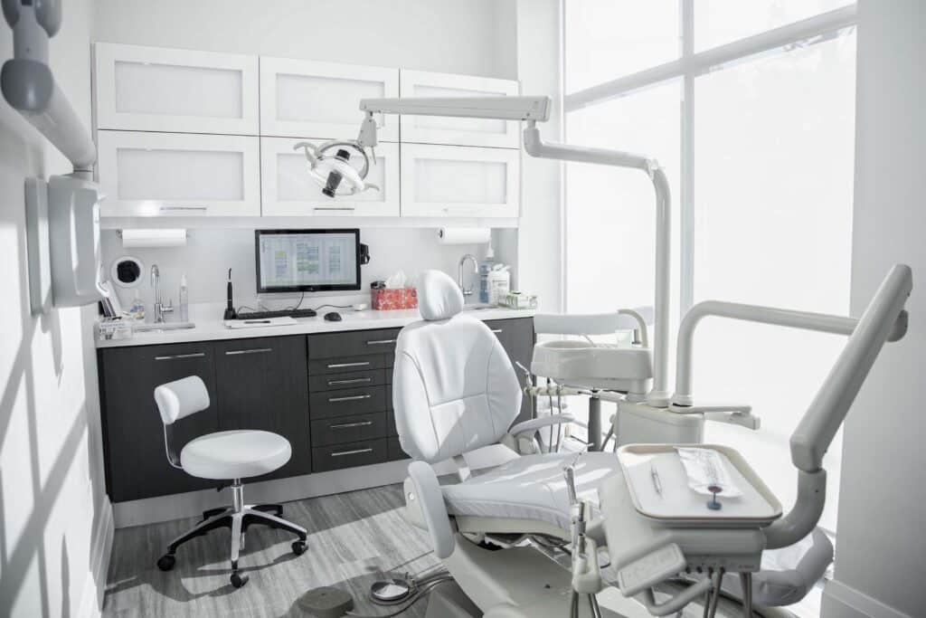 A modern dental office featuring an examination chair, equipment, and a workstation with a computer, all set in a bright, clean environment.