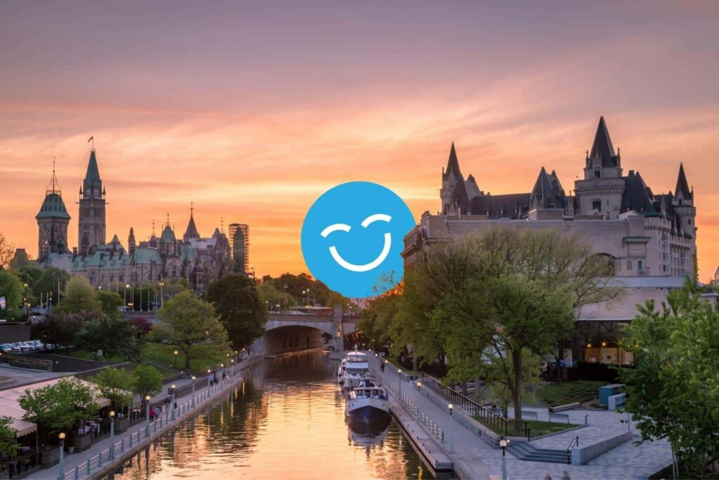 A scenic view of a city at sunset, featuring historical buildings along a river, with trees and boats in the foreground. A blue smiling face icon is superimposed at the center.