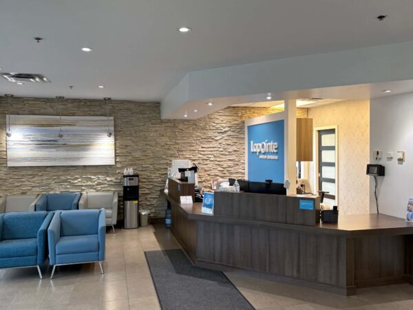 A modern reception area featuring a wooden front desk, seating in light blue chairs, and a stone accent wall. Brightly lit with natural light, it creates a welcoming atmosphere for visitors.