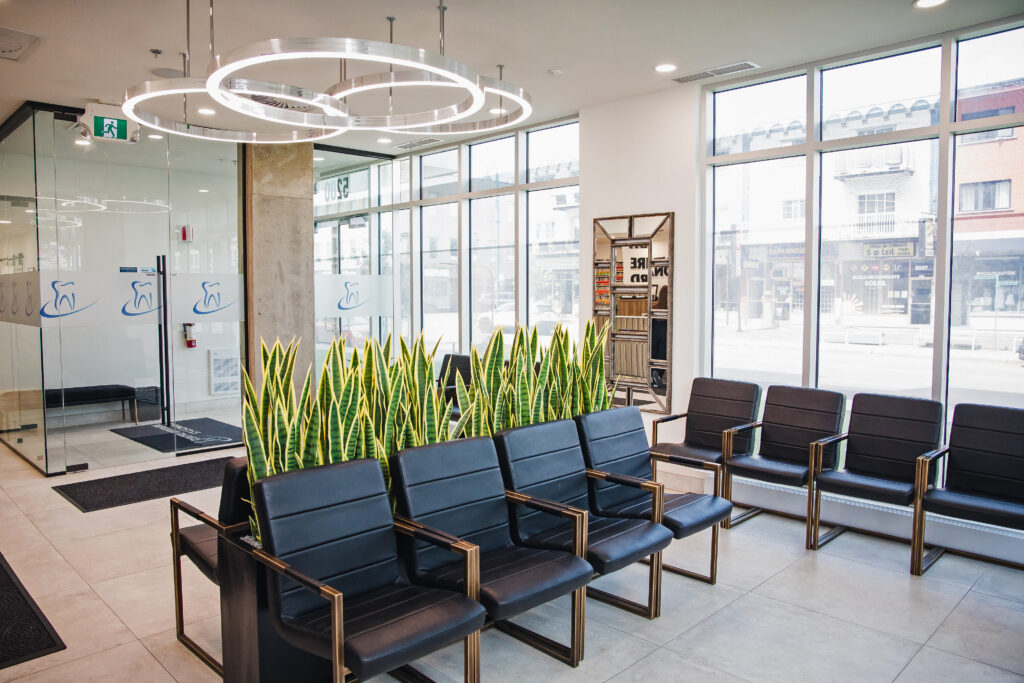 A modern dental office reception area featuring stylish seating, large windows for natural light, and decorative plants. The space is welcoming and inviting, designed for patient comfort.