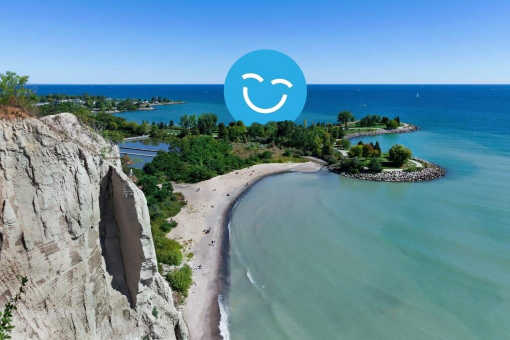 A scenic view of a sandy beach and turquoise waters surrounded by lush greenery, with a bright blue sky overhead and a smiling face icon superimposed on the image.