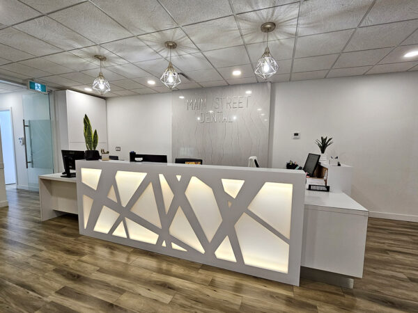 A modern dental office reception area featuring a bright, welcoming design with a stylish front desk illuminated by soft lighting. The space includes sleek furniture, plants, and a professional atmosphere, inviting patients to feel at ease. The friendly 123Dentist Smiley adds a cheerful touch.